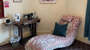 Habitación de esquina con cama, una máquina de coser, una mesa con hervidor, un televisor y un cuadro en la pared.