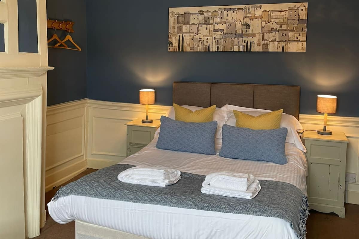 A neatly arranged bedroom with a large bed, two bedside tables with lamps, a decorative ceiling light, and a cityscape painting on the wall.