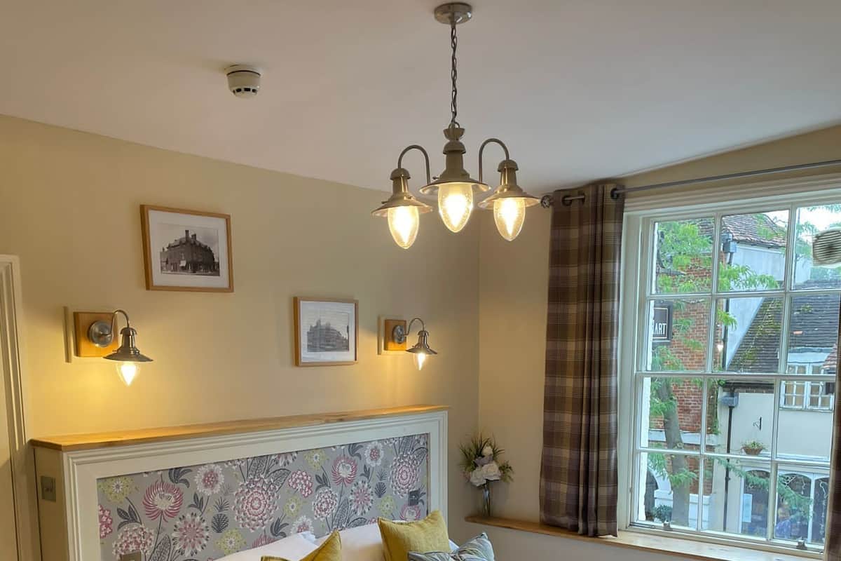 A bedroom with a wooden bed, floral wallpaper, a window with a view, and wall-mounted lights.