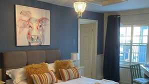 Habitación de hotel con una cama grande, un cuadro en la pared, una araña, un escritorio y una ventana con cortinas.