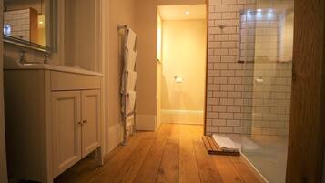 A bathroom with wooden flooring, a glass shower enclosure, and a white tiled wall.