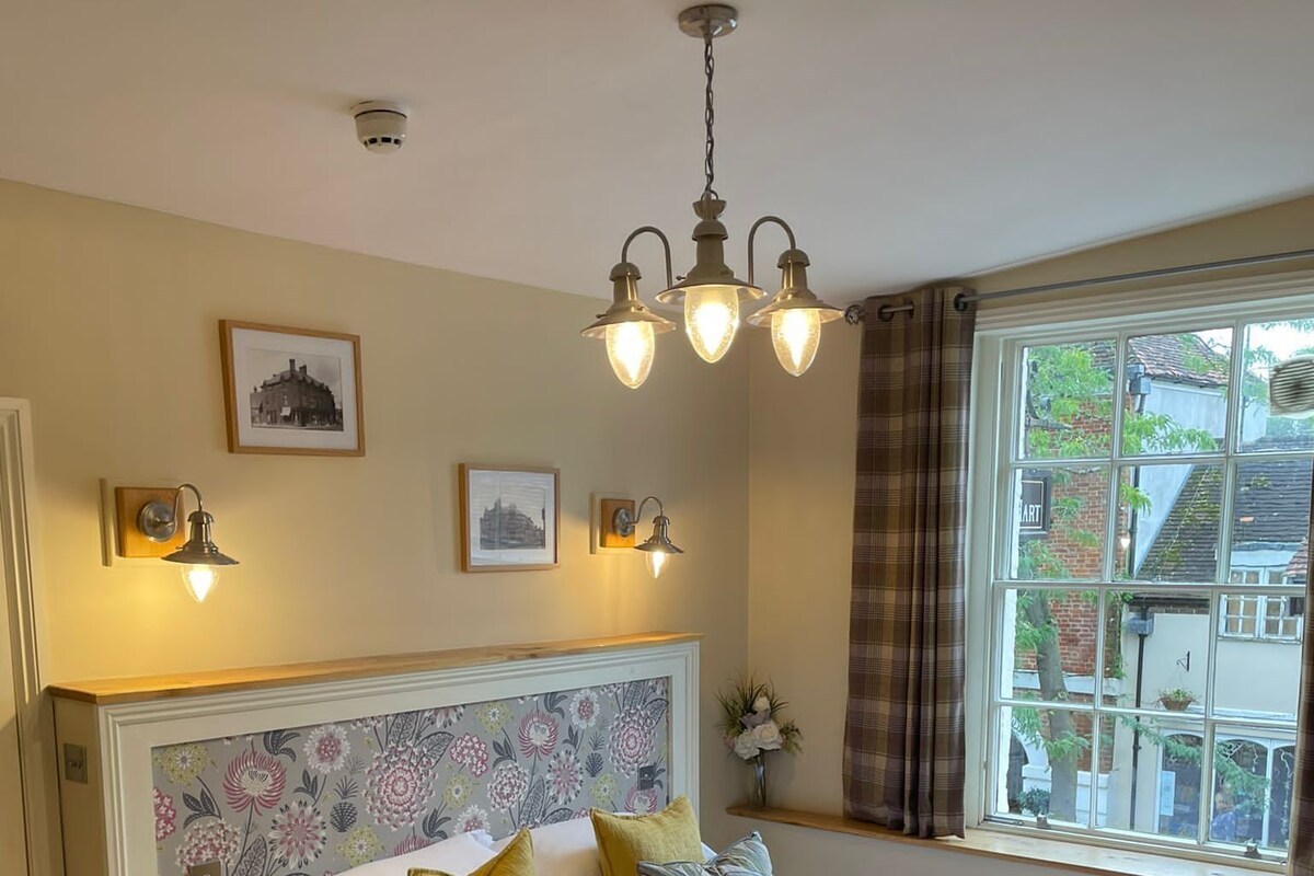 A bedroom with a wooden bed, a headboard with floral wallpaper, a window with a view, and wall-mounted lights.