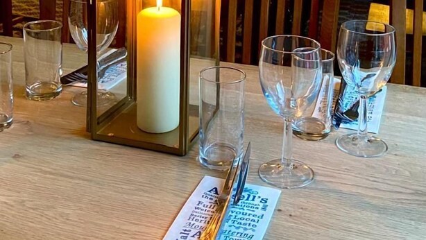 Un comedor con una mesa preparada para una comida, que incluye una vela, vasos y una carta.