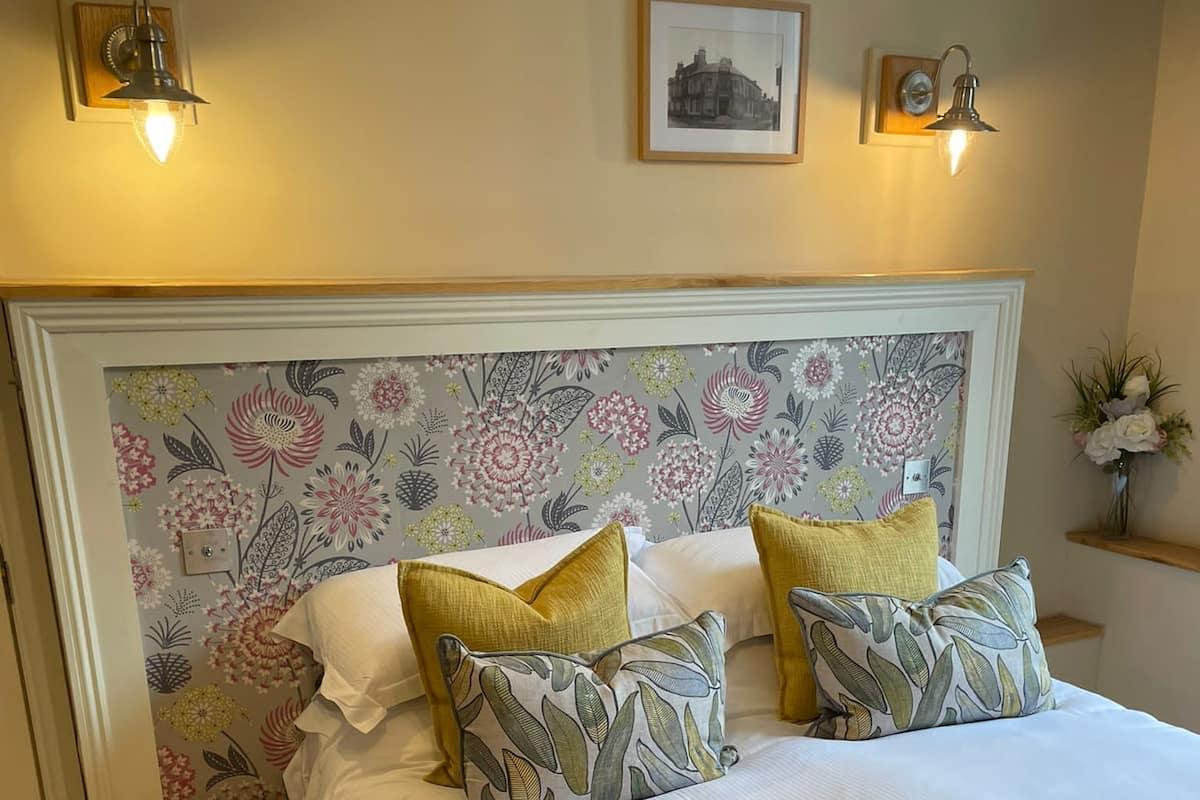 A neatly made bed with floral-patterned headboard, bedside tables, and wall-mounted lamps.