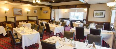Ein Restaurant mit mehreren Esstischen, Holzbalken an der Decke und einem karierten Teppich.