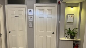 A hallway with two white doors, one labeled "Rooms 6-9" and the other "Rooms 1-5". There are signs indicating Wi-Fi availability and a notice that rooms are serviced on request. A fire extinguisher is mounted on the wall to the right. - Geminian Guest House (Harrogate)