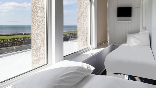 A hotel room with two beds, a TV, and a view of the sea. - Harlands Hotel (Blackpool)