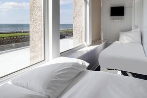 Habitación de hotel con dos camas, televisión y vista al mar.