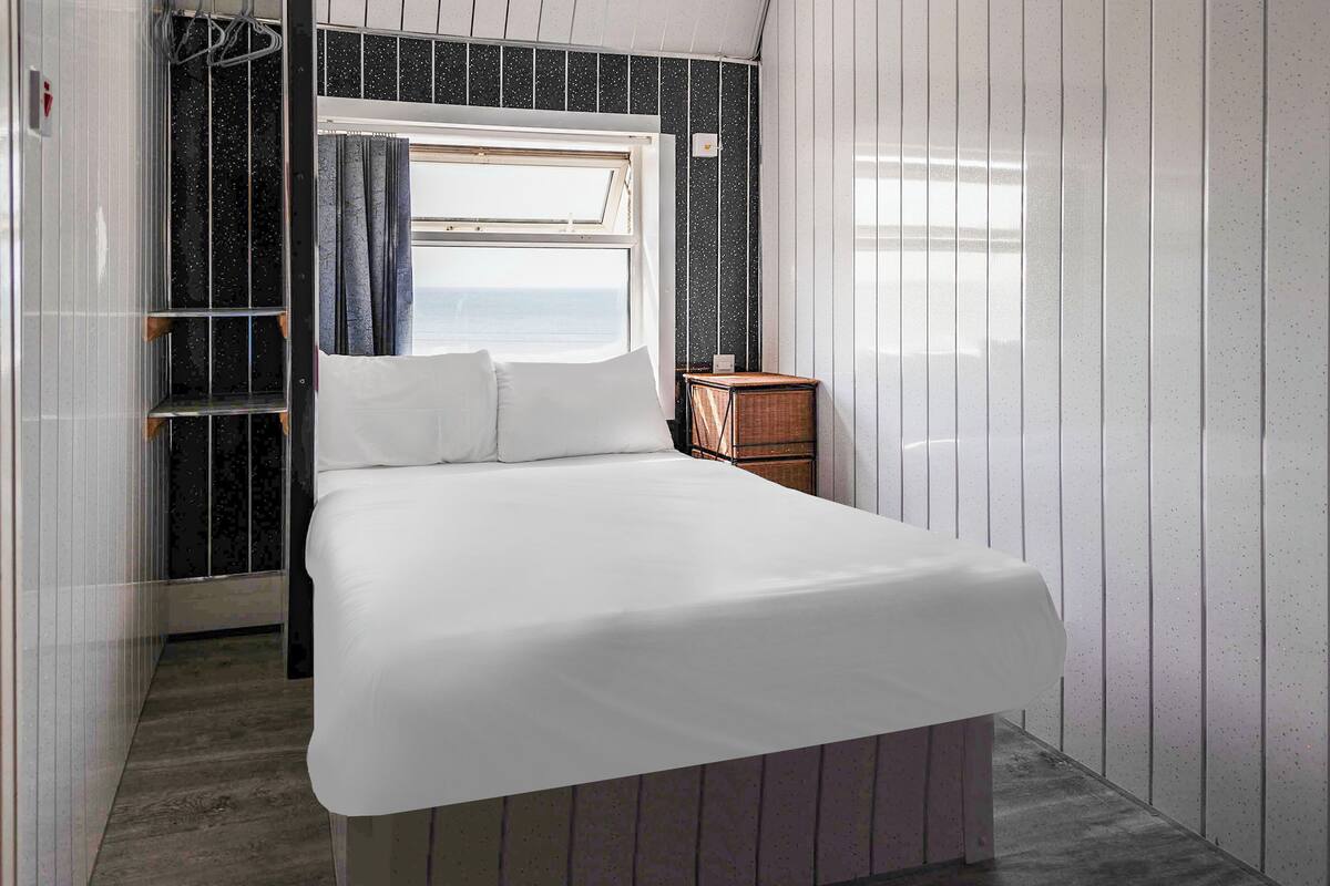 A bedroom with a bed, a window, and a small wooden nightstand.
