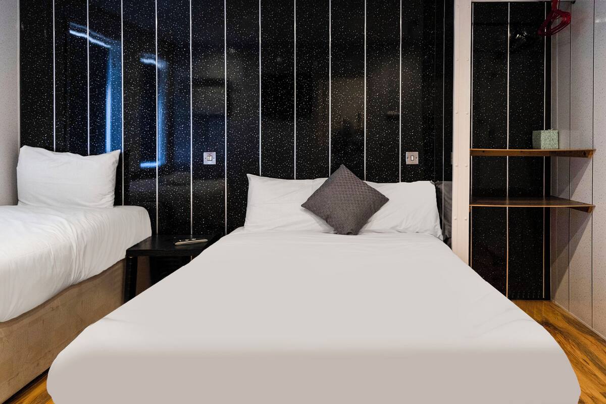 A bedroom with a large bed, two bedside tables, a wardrobe, and a starry night sky view through the window.