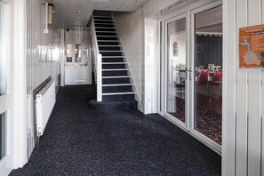 Stairs lead to a room with a radiator and a door, adjacent to a dining area with chairs.