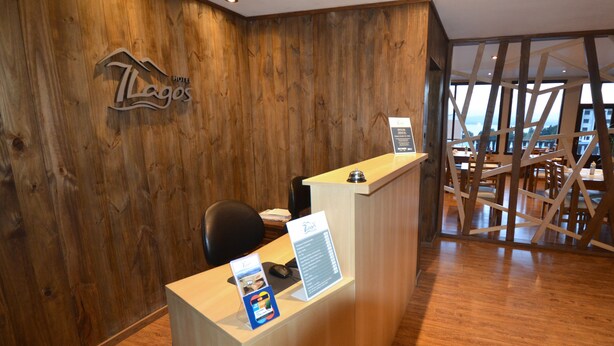 Ein Hotelrezeptionstresen mit einer Holzwand, einem Schild mit der Aufschrift 'LaGos Hotel' und Blick in den Speisesaal durch eine Glasscheibe.