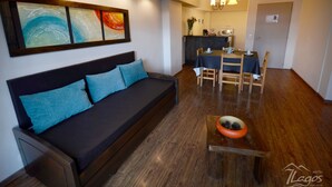 Ein modernes Wohnzimmer mit einem dunklen Sofa, Holzboden und einem Essbereich mit Tisch und Stühlen.