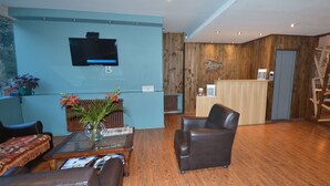 Eine Hotelhalle mit Rezeption, Sitzgelegenheiten und einem an der Wand montierten Fernseher.