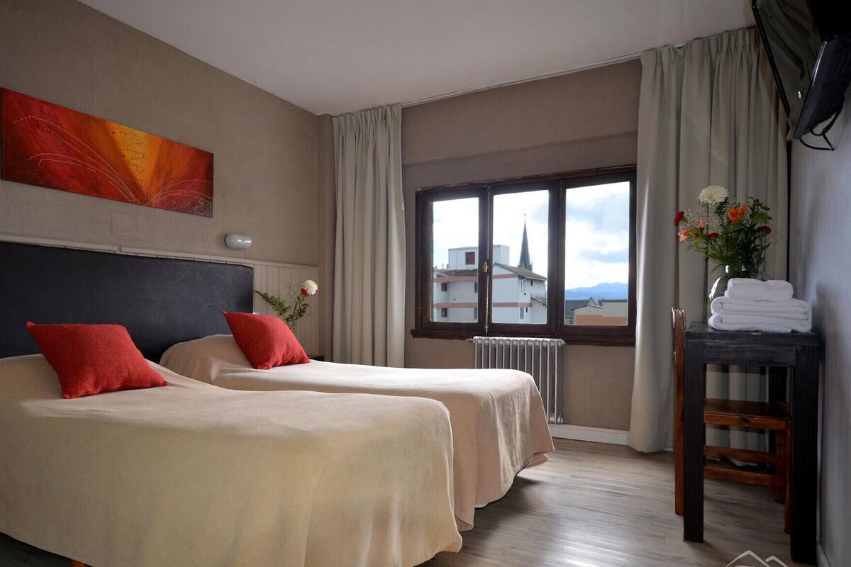 A hotel room with two beds, a window with a view, a radiator, and a table with towels.