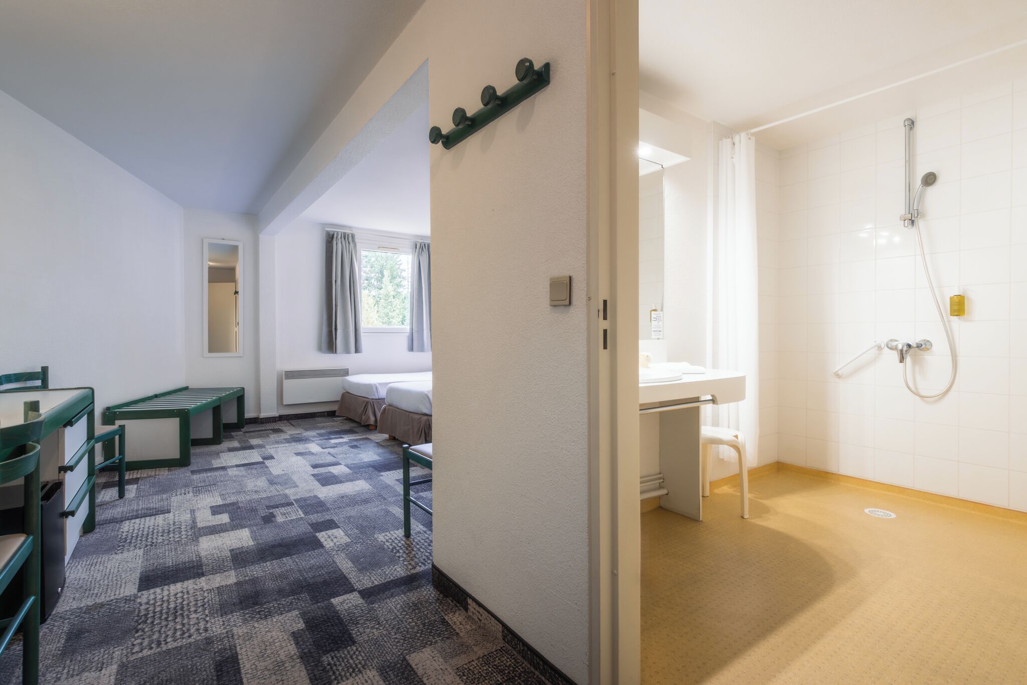 Una habitación de hotel con cama, escritorio, baño con ducha y ventana con cortinas.