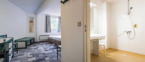 Una habitación de hotel con cama, escritorio, baño con ducha y ventana con cortinas.