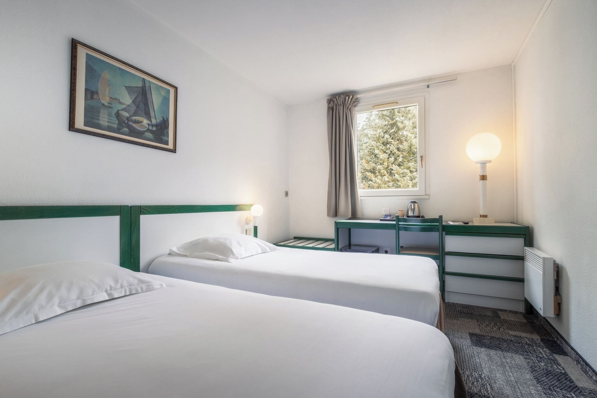 Une chambre d’hôtel avec deux lits, un bureau, une lampe, un tableau et une fenêtre avec des rideaux.