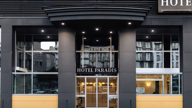 Una entrada de hotel moderna con fachada de vidrio, un llamativo letrero 'HOTEL PARADIS' y un interior visible a través del cristal.