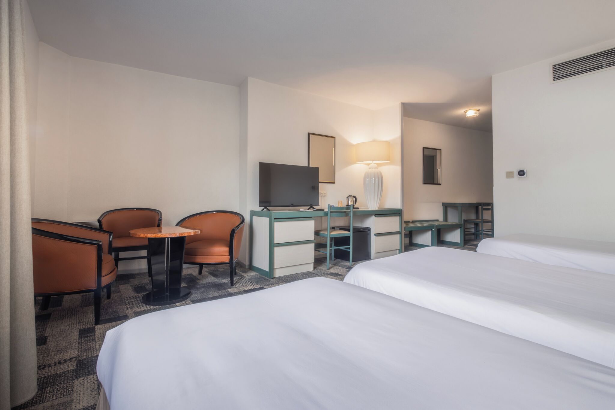 A hotel room with two beds, a desk, a chair, a television, and a lamp.
