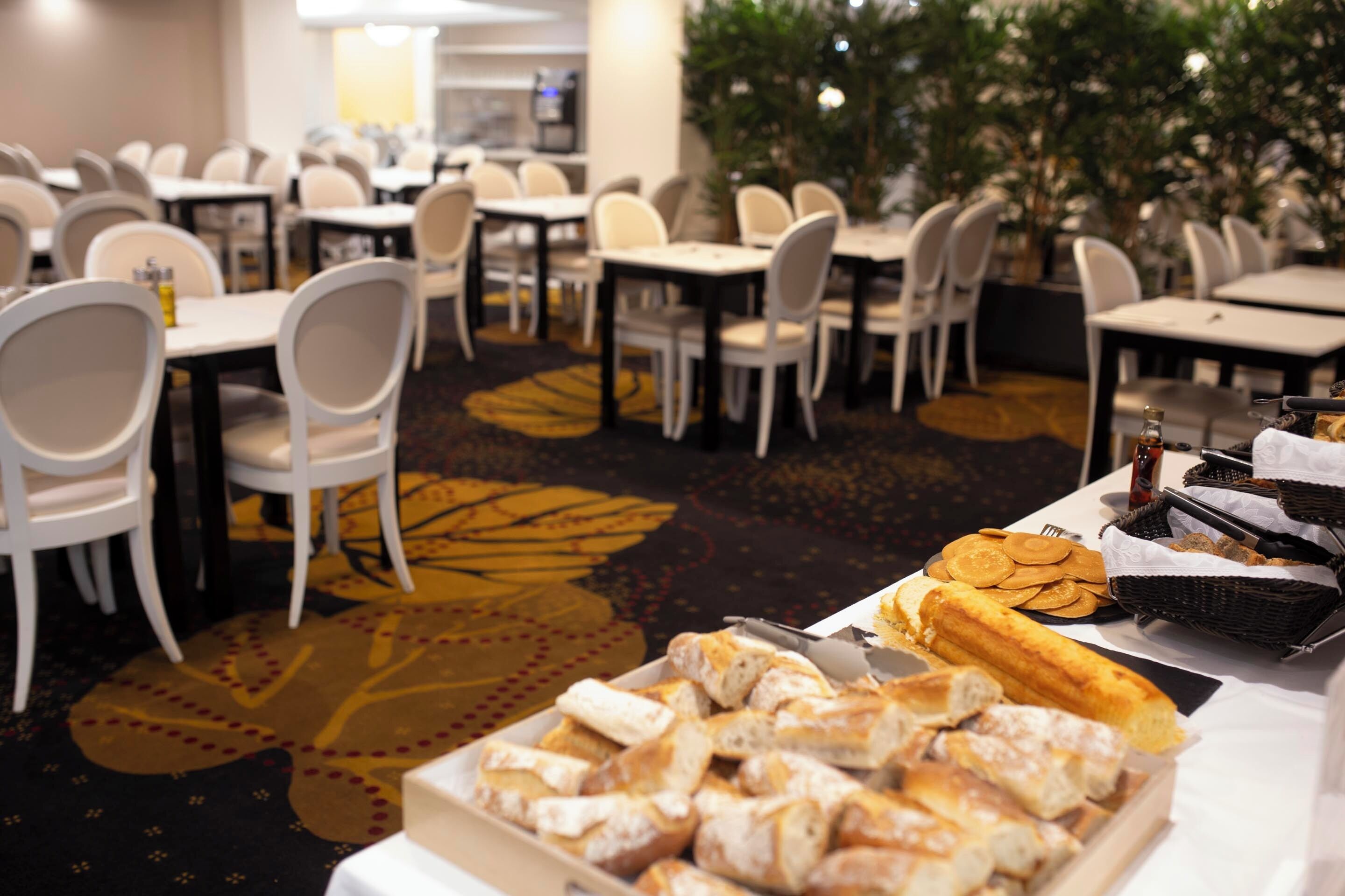 A buffet setup with various pastries and bread, arranged on tables in a dining area with chairs and tables.