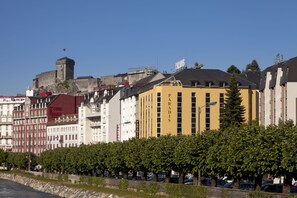 A historic building with a tower, surrounded by modern buildings with visible signage. - Hotel Paradis (Lourdes)