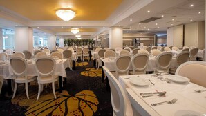 Un salón de banquetes con varias mesas redondas, sillas blancas y una alfombra estampada con motivos florales.