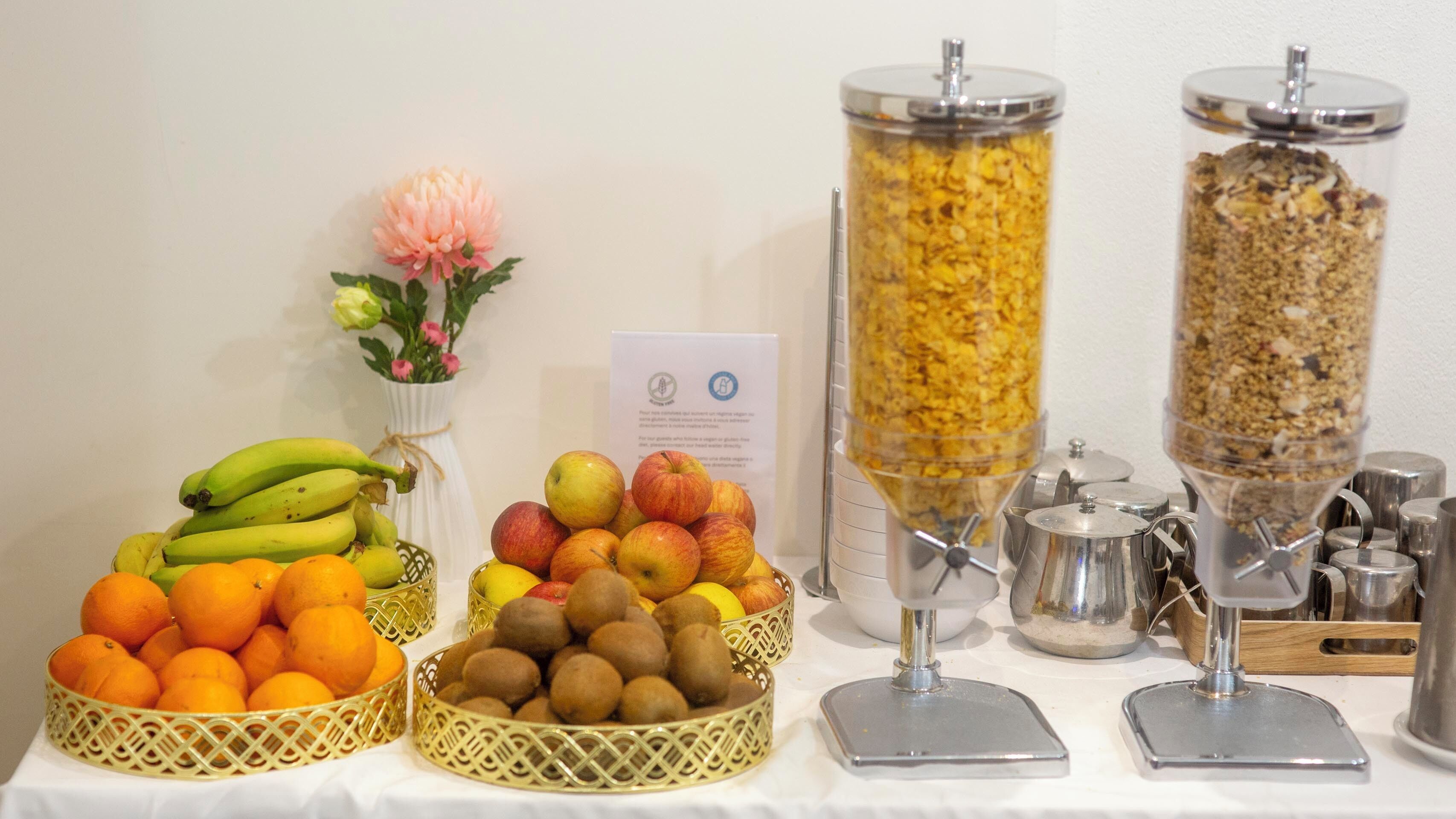 A buffet table with various fruits and a granola dispenser.