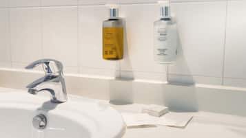 Baño con lavamanos blanco, grifo cromado y dos botellas de jabón líquido Aqua Senses sobre una repisa.