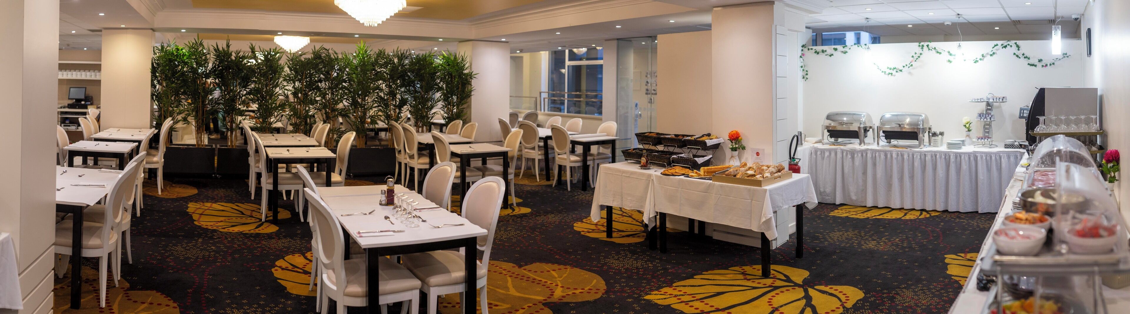 A dining area with tables set for a meal, a buffet line with various food items, and a coffee station.