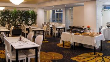 A dining area with tables set for a meal, a buffet line with various food items, and a coffee station.