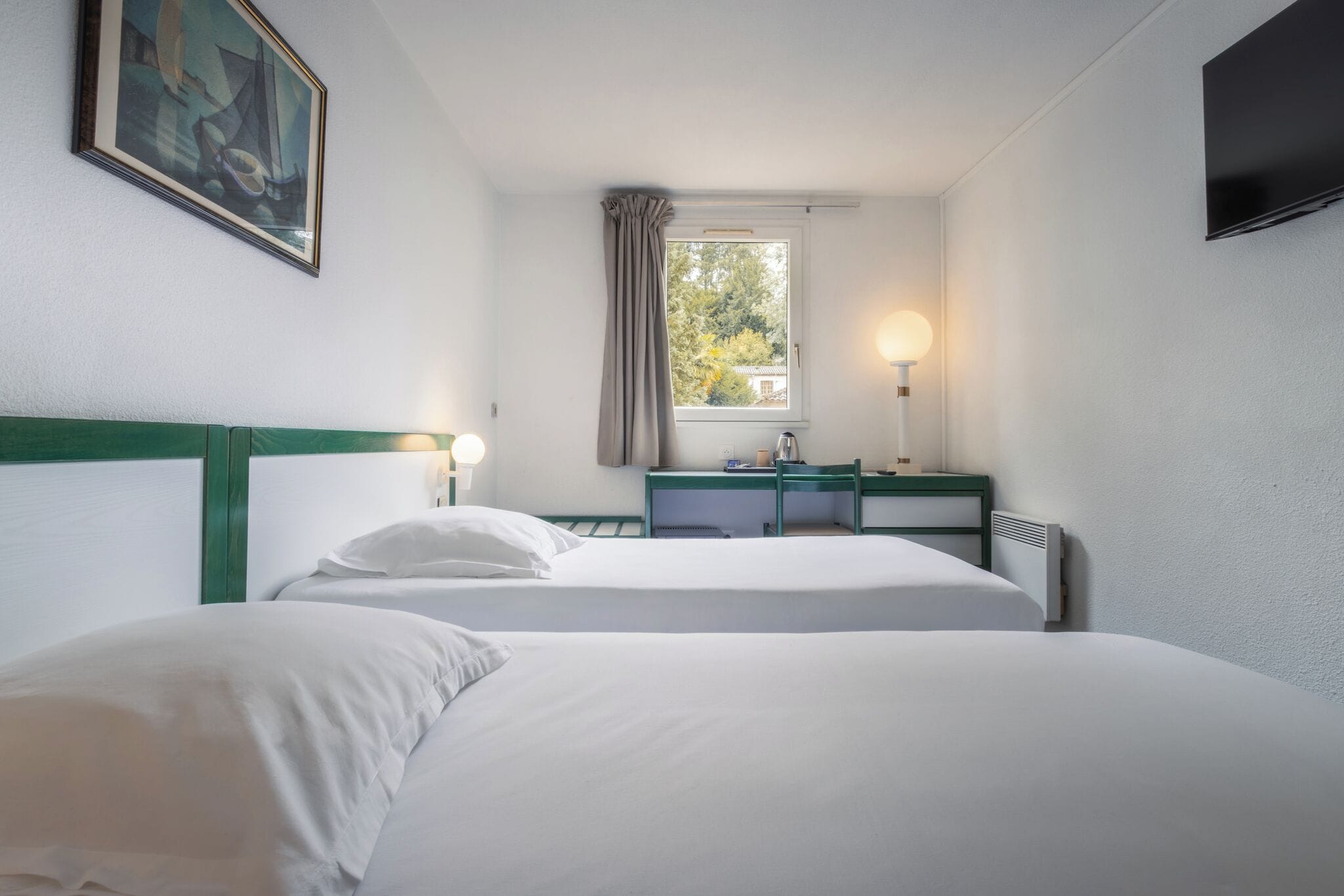 A hotel room with two beds, a desk, a chair, a TV, a window with curtains, and a painting on the wall.