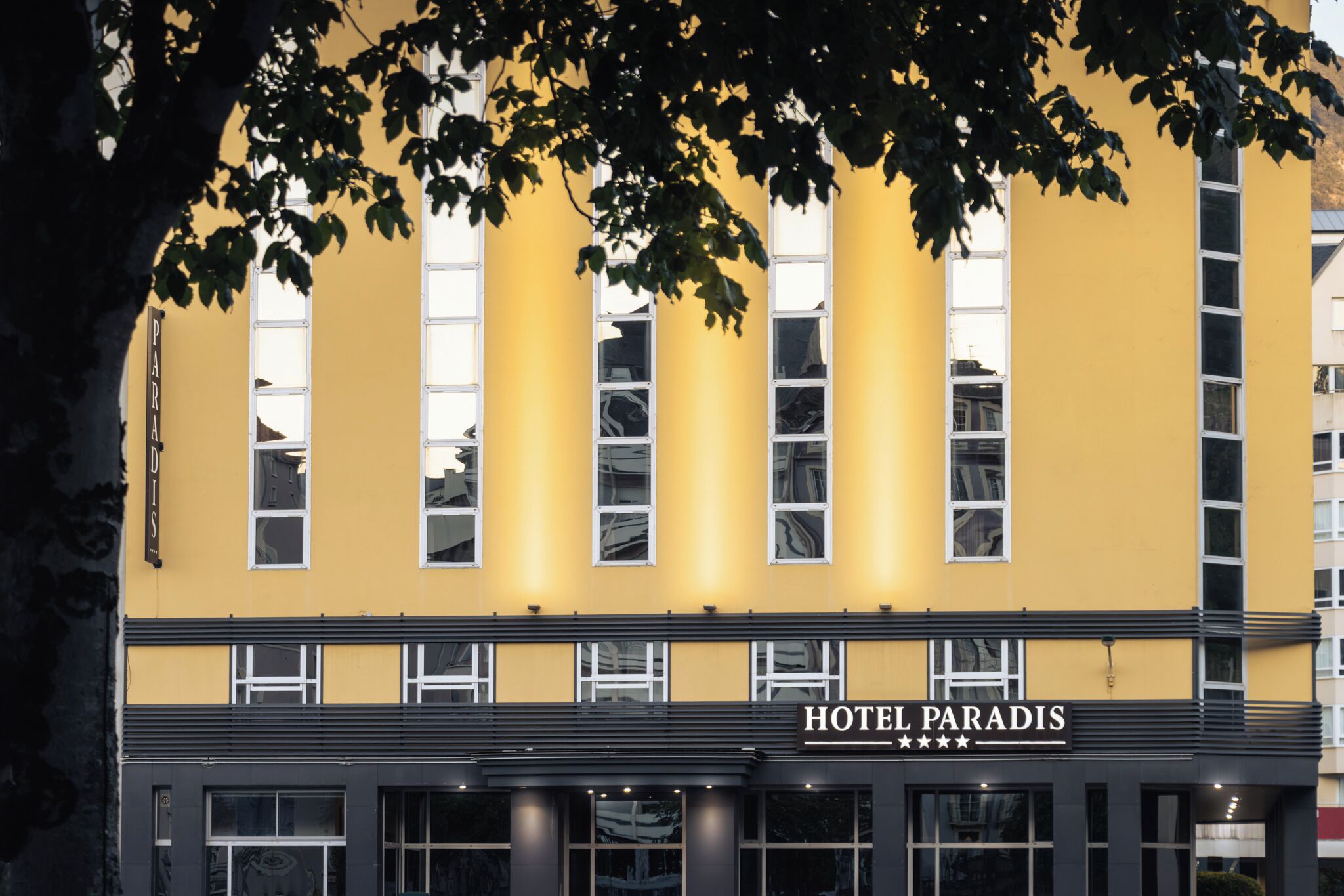 Ein Hotel mit gelber Fassade, zahlreichen Fenstern und einem Schild mit der Aufschrift 'HOTEL PARADIS'.