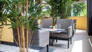 Un área de comedor al aire libre con mobiliario de mimbre, una mesa con una botella y vasos, y plantas en macetas.