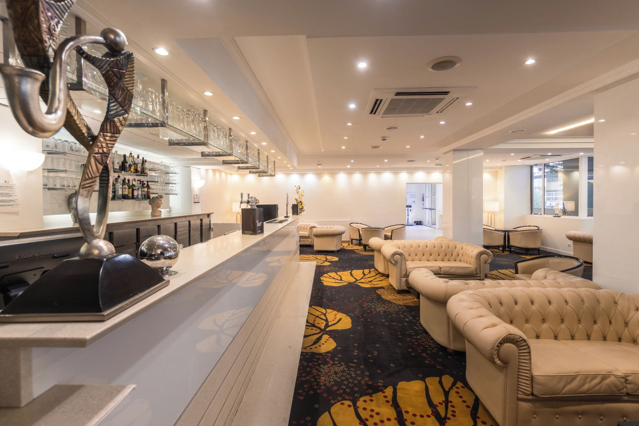 A hotel lobby with a bar area, seating, and a patterned carpet.