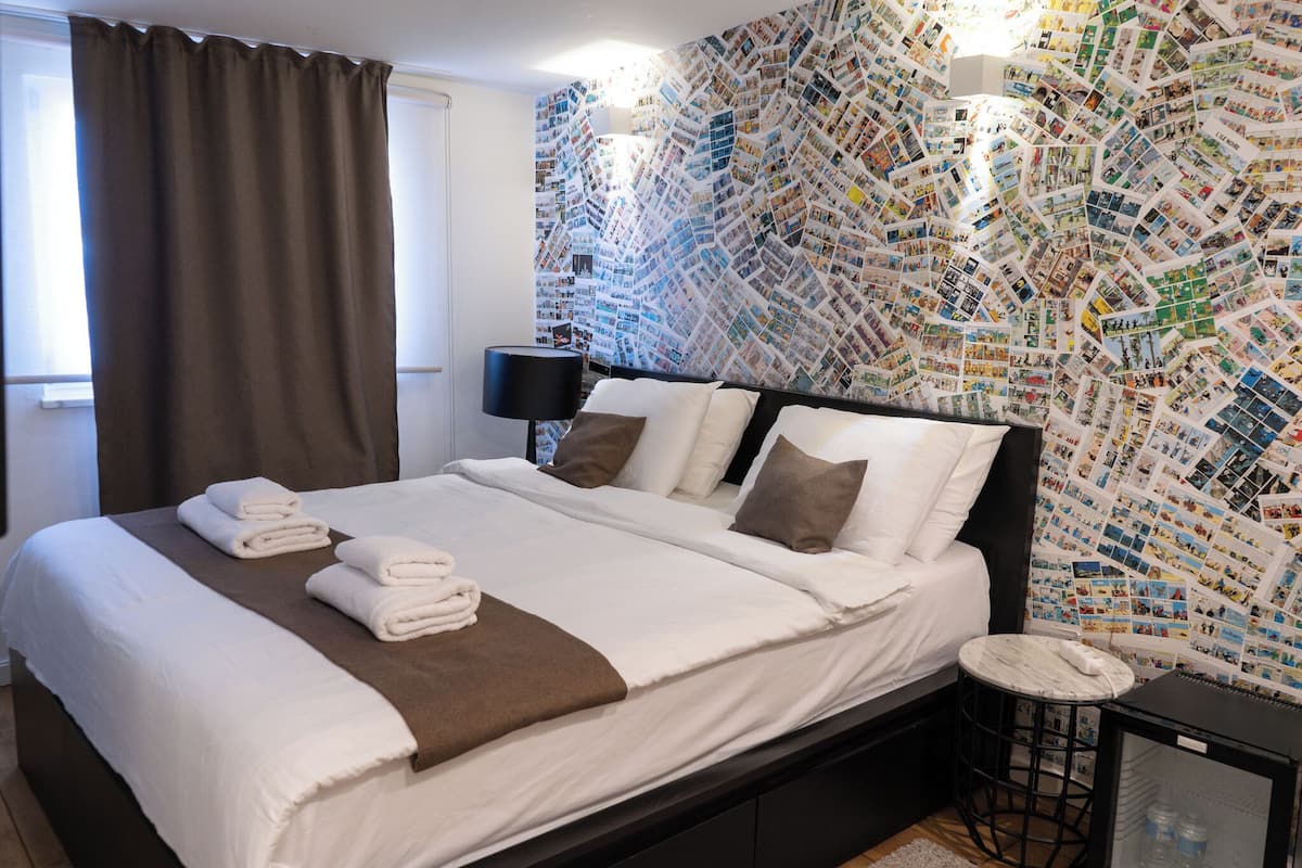 A neatly made bed with white and brown linens, a bedside table with a lamp, and a wall covered with a collage of photos.