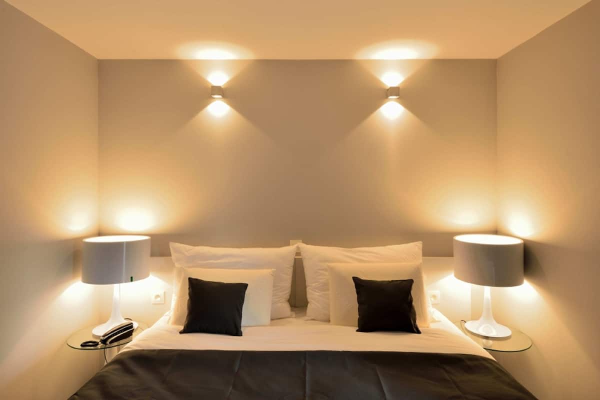 A hotel room with a bed, two bedside lamps, and a nightstand with a book and glasses.