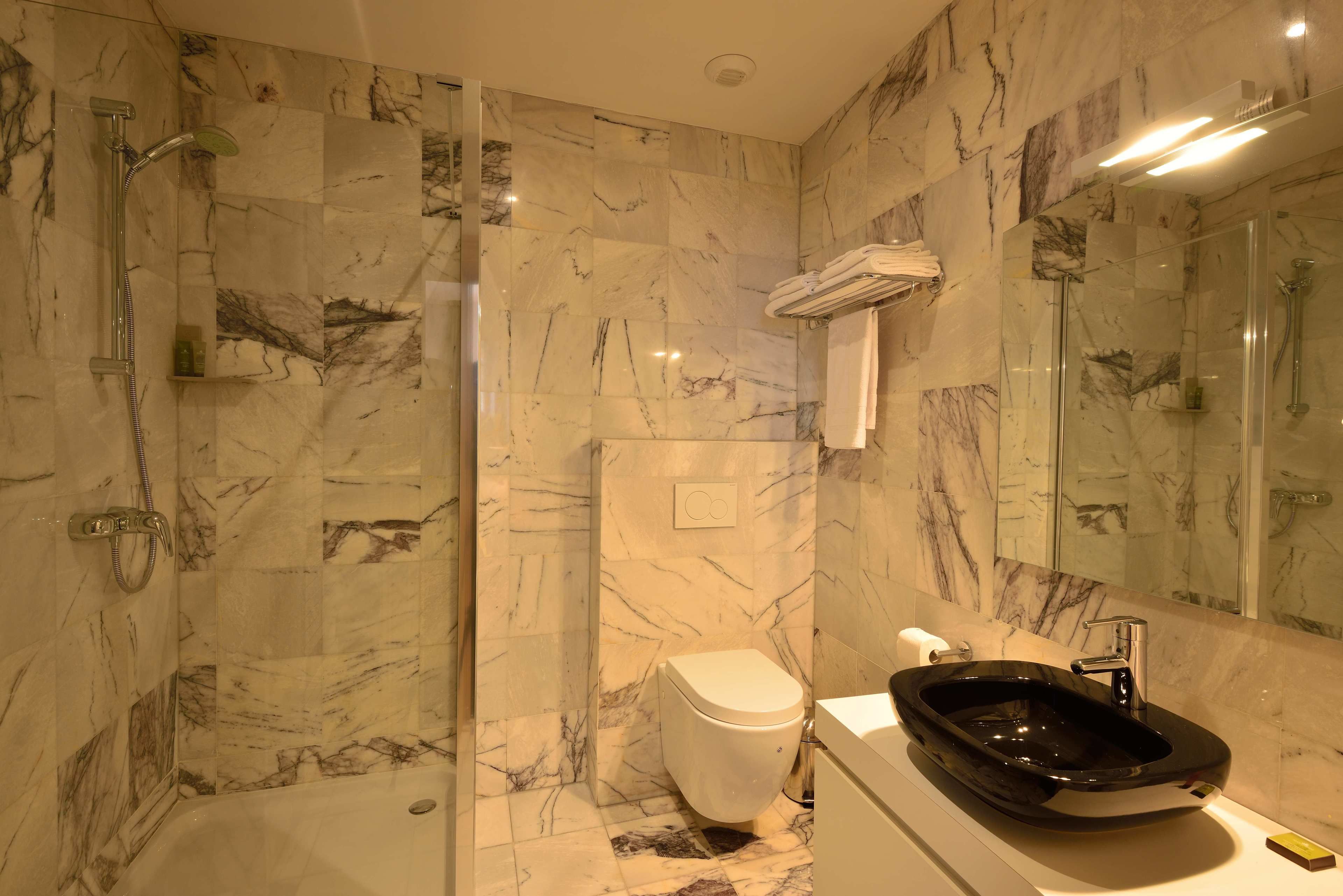 A bathroom with a marble wall, a black sink, a toilet, and a shower area.