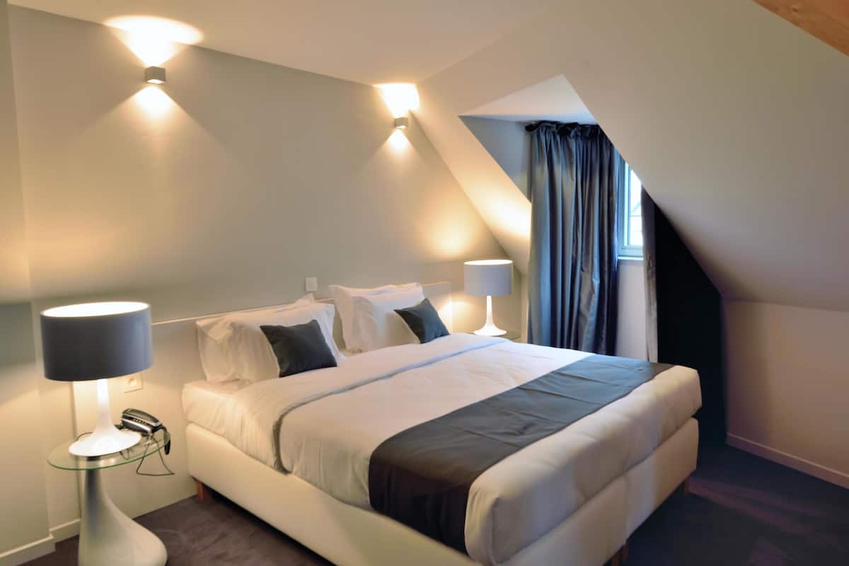 A modern bedroom with a bed, two bedside lamps, a telephone, and a glass table.