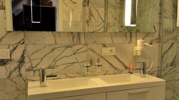 Un baño moderno con paredes de mármol, un mueble de tocador con doble lavabo y un espejo grande.