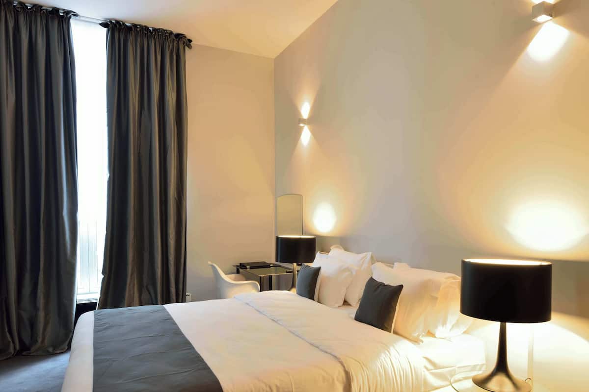 A hotel room with a bed, bedside table, lamp, and a chair.