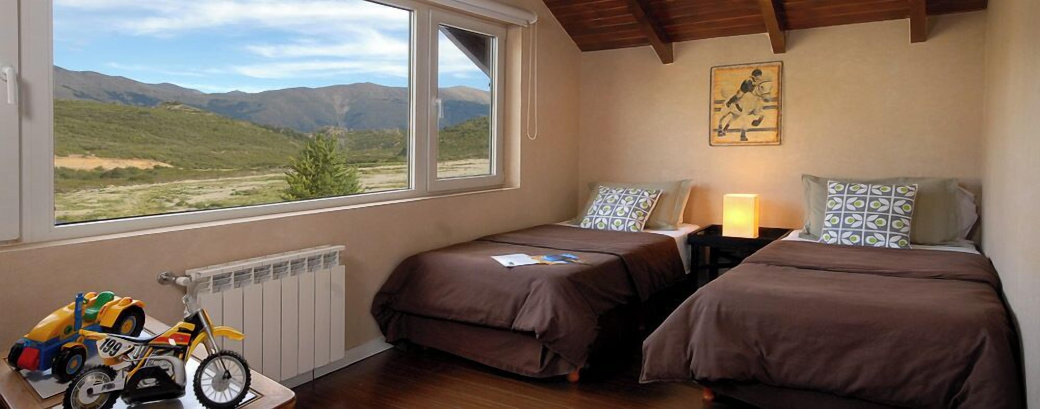 Un dormitorio con dos camas, una ventana con vistas a montañas, un radiador y una motocicleta de juguete.
