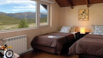 Un dormitorio con dos camas, una ventana con vistas a montañas, un radiador y una motocicleta de juguete.