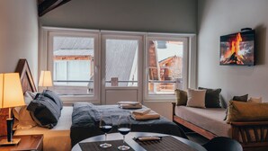 A hotel room with a bed, bedside table, two windows, a sofa, and a TV on the wall. - Ski Sur Apartments (San Carlos de Bariloche)