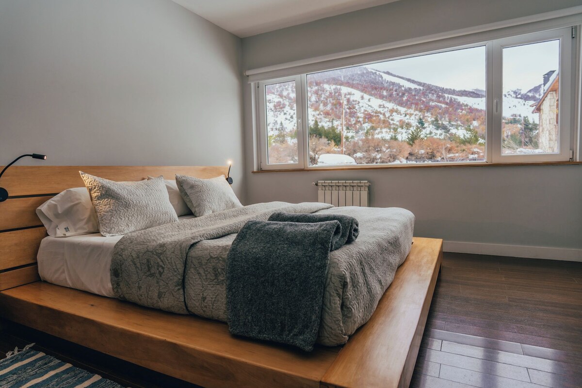 A bedroom with a bed, a window with a view of a snowy landscape, and a radiator.