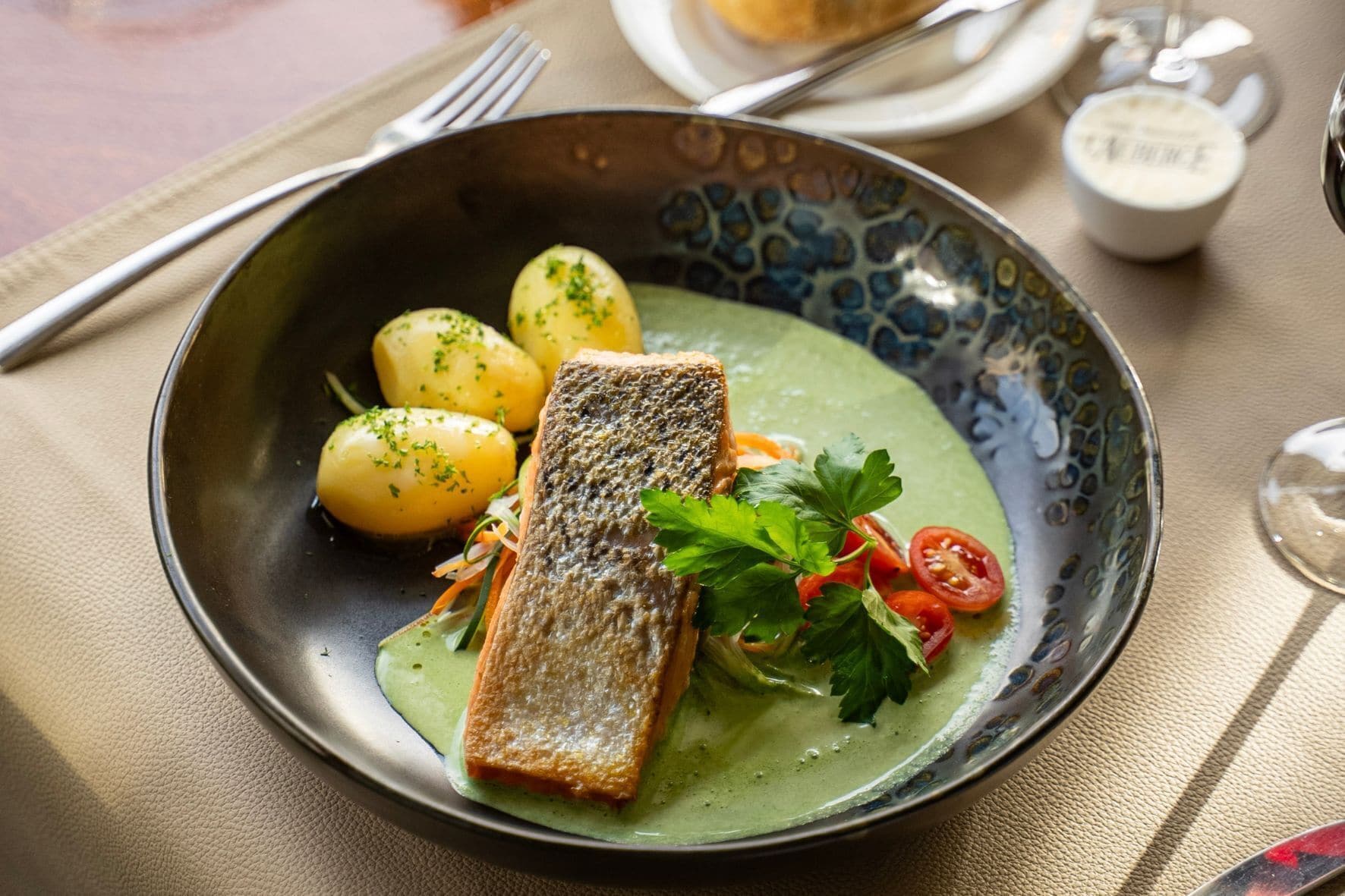 Un plato de comida con un trozo de pescado, patatas y guarniciones.