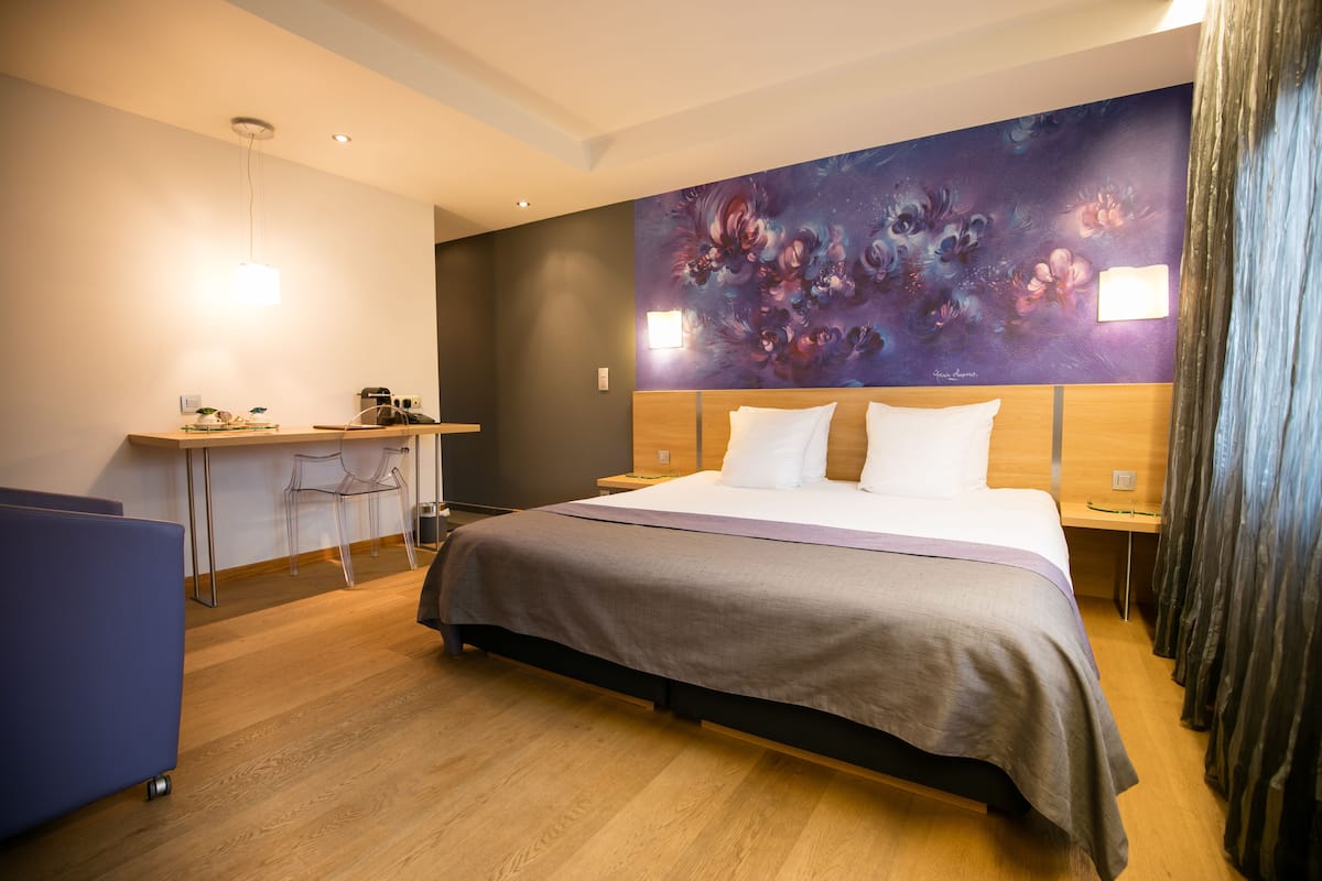 A modern hotel room with a large bed, a desk, and a chair.