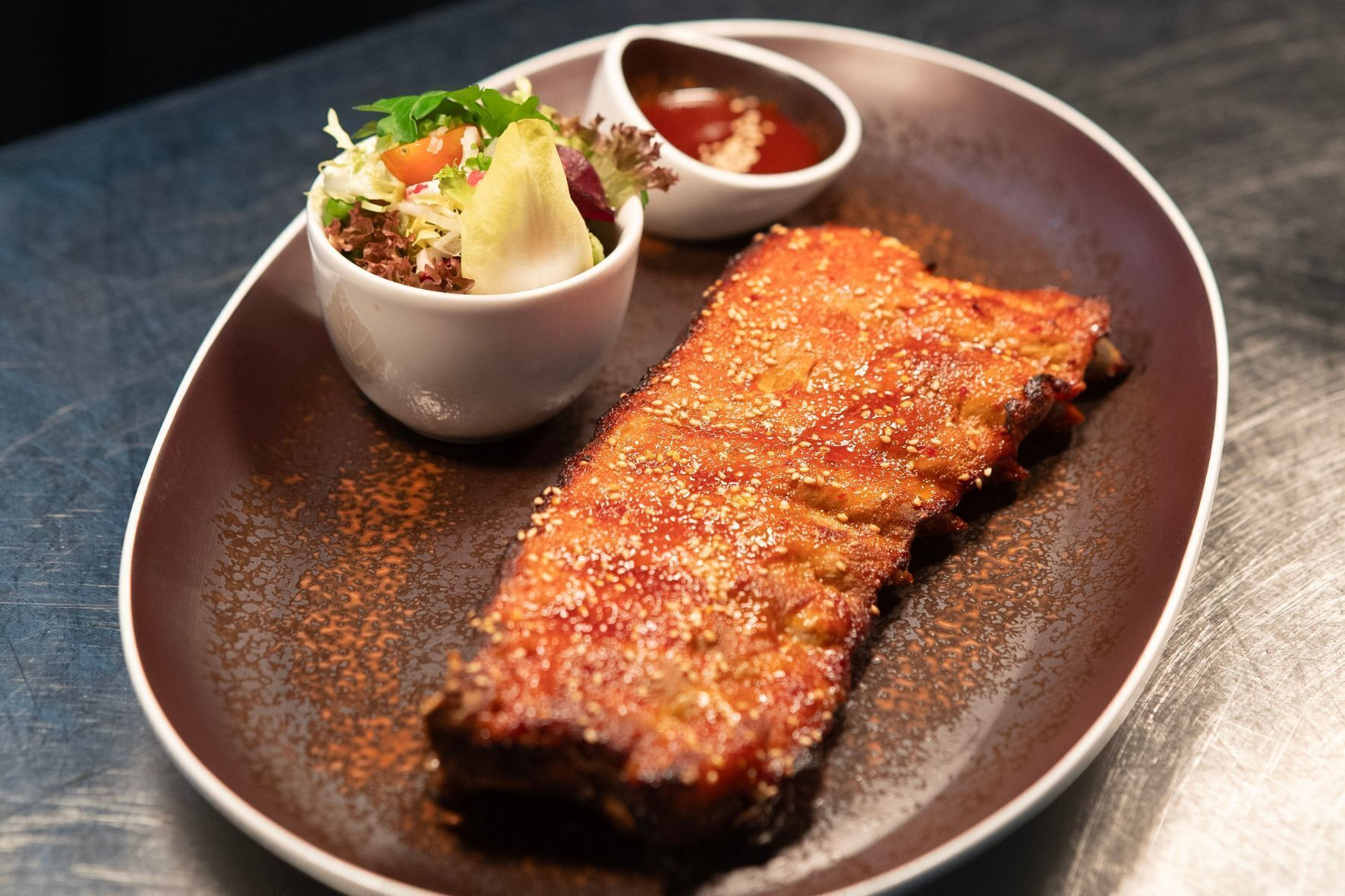 A plate with a crispy, seasoned fish fillet, a small bowl of salad, and a side of sauce.