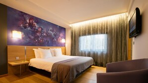 A hotel room with a large bed, a nightstand, a TV mounted on the wall, and a window with curtains. - Hôtel-Restaurant L’Auberge (Spa)