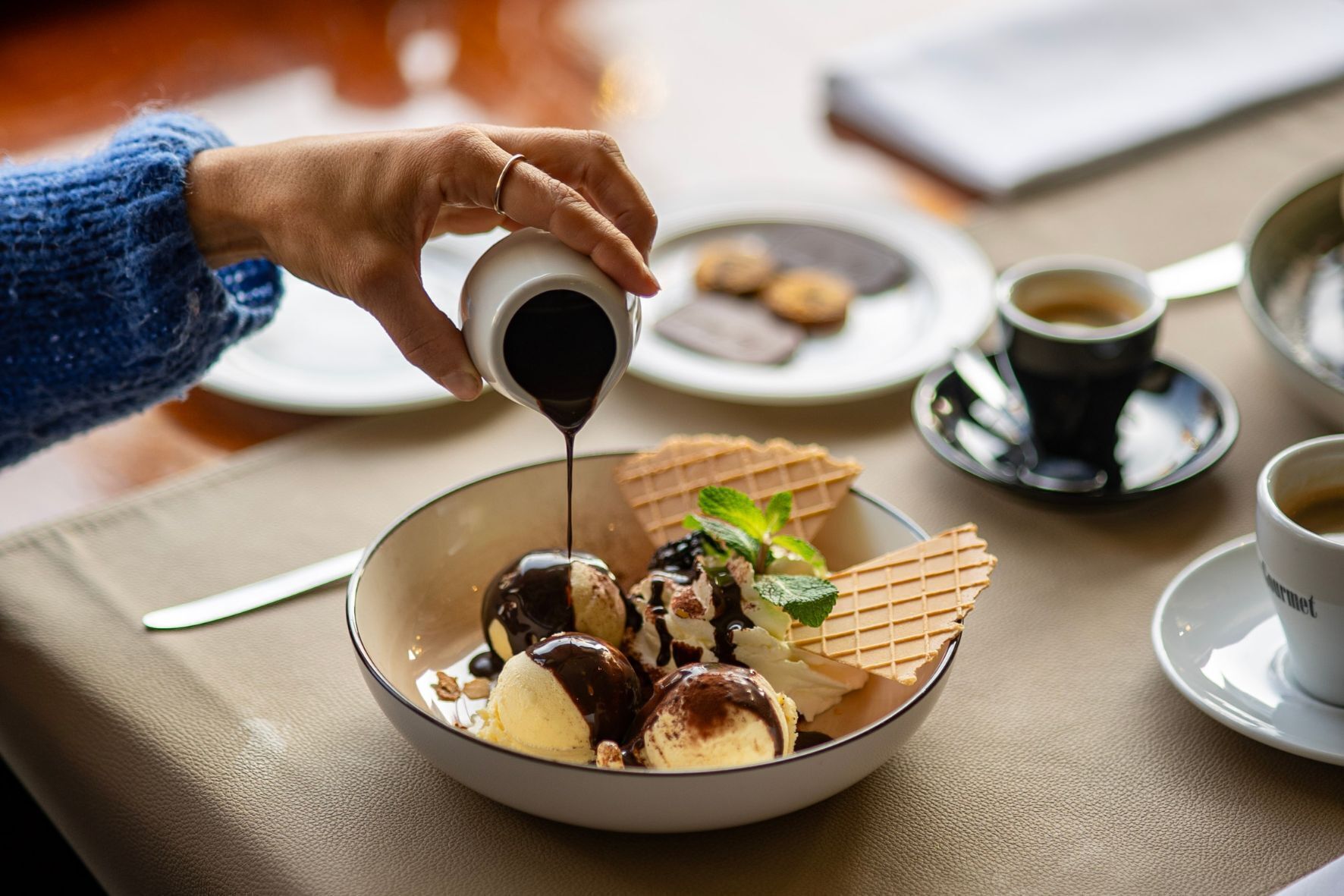Eine Schale Dessert mit Eiscreme, Schokoladensauce und Waffelkeksen auf einem Tisch.